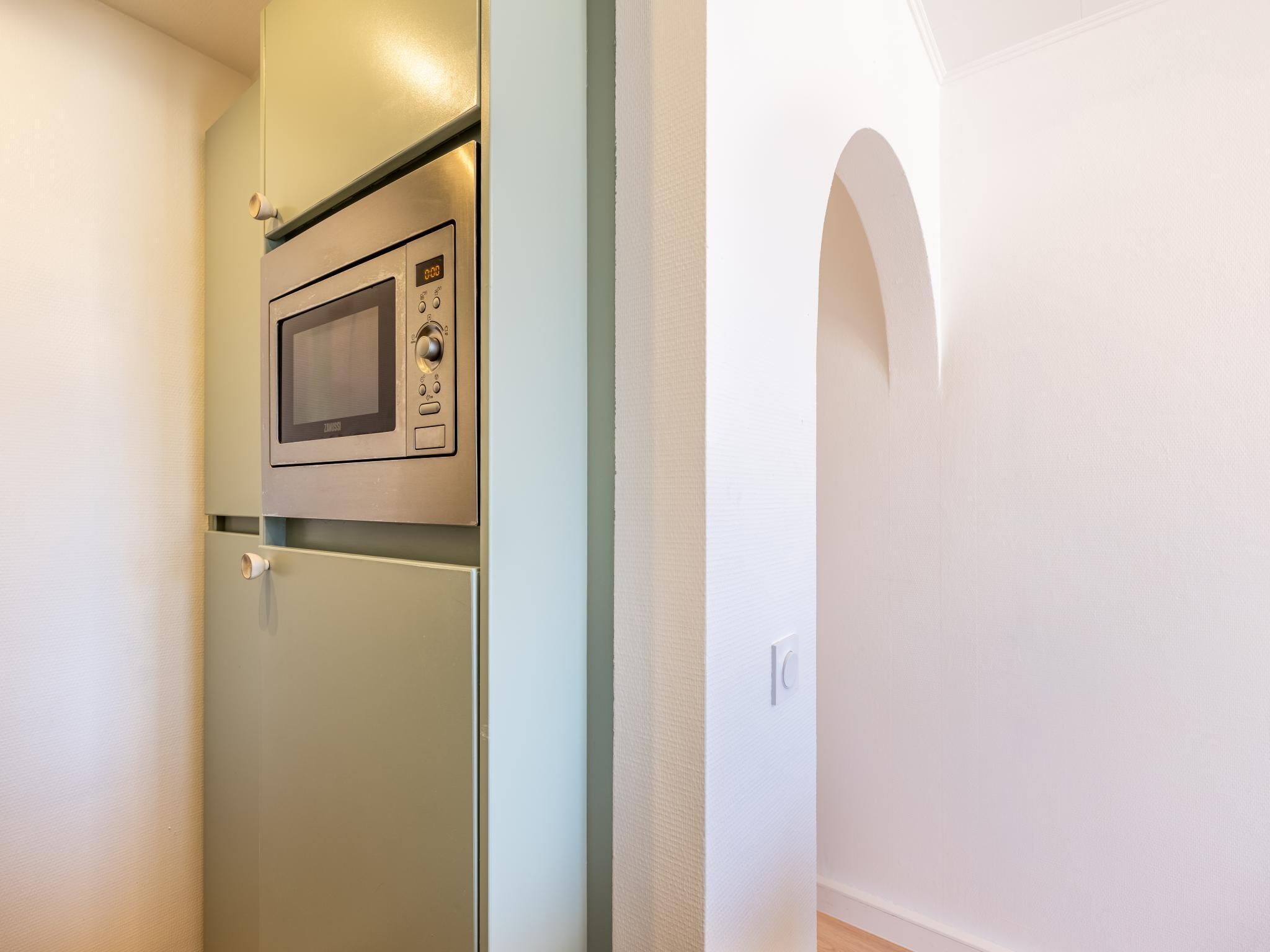 A kitchen with a microwave, a refrigerator, and a door with a handle.
