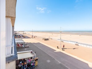 A beachside promenade with shops, a clear sky, and a sandy beach. - Tastefully furnished apartment with sea view (Koksijde)