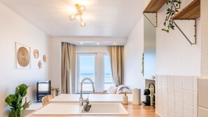 A modern kitchen with a large island, a built-in oven, and a view of the sea through the window. - Tastefully furnished apartment with sea view (Koksijde)