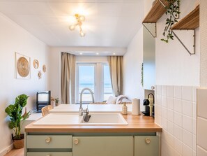 A modern kitchen with a large island, a built-in oven, and a view of the sea through the window. - Tastefully furnished apartment with sea view (Koksijde)