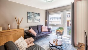 A modern living room with a sofa, coffee table, and artwork on the wall. - Cozy apartment & terrace, 100 m from sea (Koksijde)