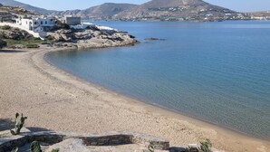 A coastal beach with a clear view of the sea, a rocky shoreline, and a small building with a white facade. - Paros Studio 8th Central Naousa (Naousa)