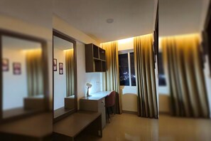 Quarto de hotel com escrivaninha, cadeira, espelho e janela com cortinas.
