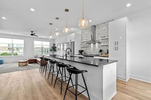 Une cuisine moderne dotée d’un îlot central, de tabourets de bar, de luminaires suspendus et d’une grande fenêtre.