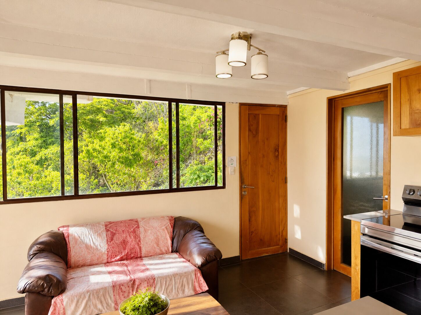 Habitación con sofá, mesa de comedor, zona de cocina y un amplio ventanal con vista a zonas verdes.