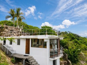 Ein weißes Gebäude mit Balkon, Treppe und Blick auf die umliegende Grünfläche und Hügel.