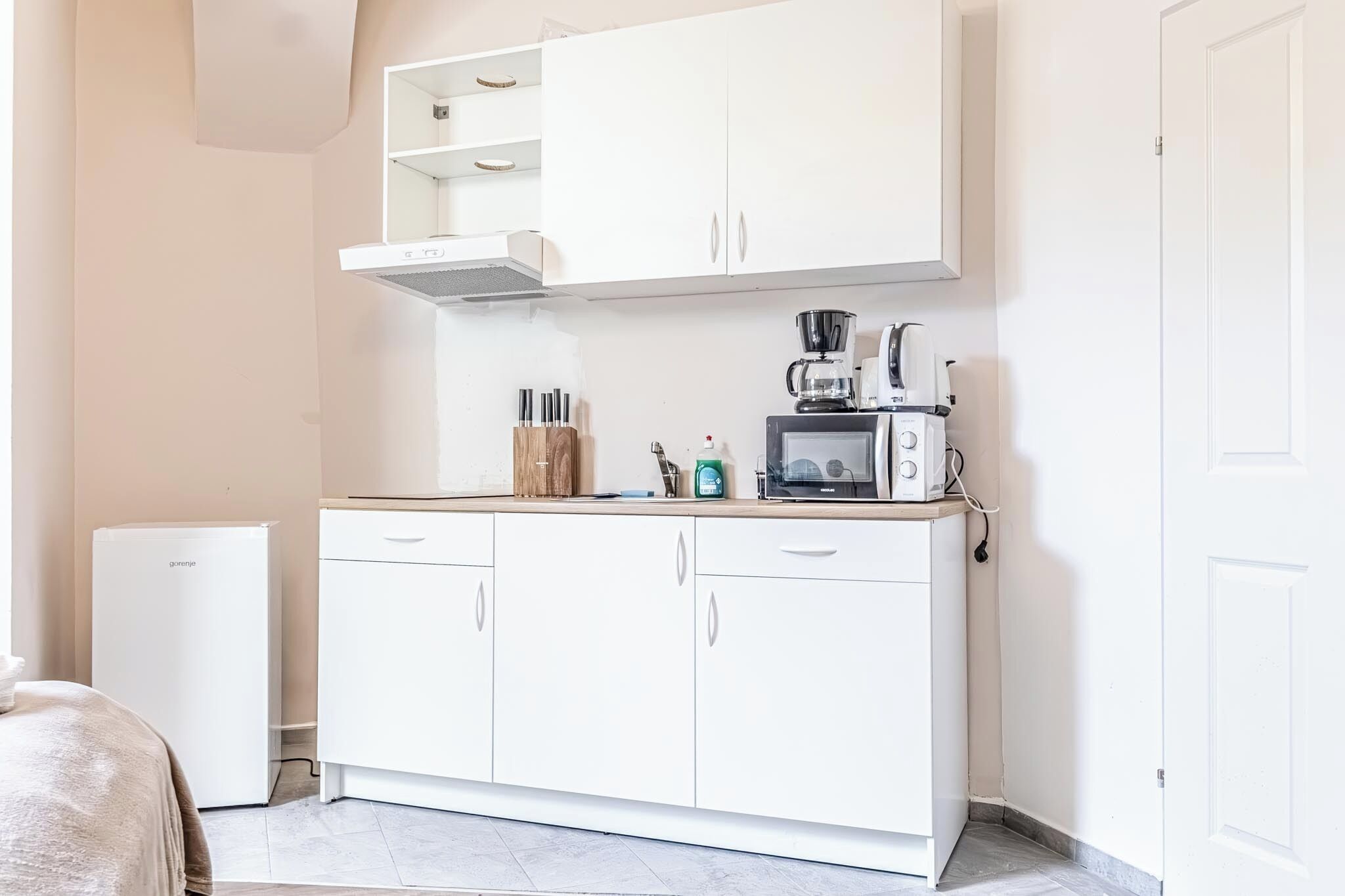 A compact kitchenette with a microwave, coffee maker, and storage cabinets.