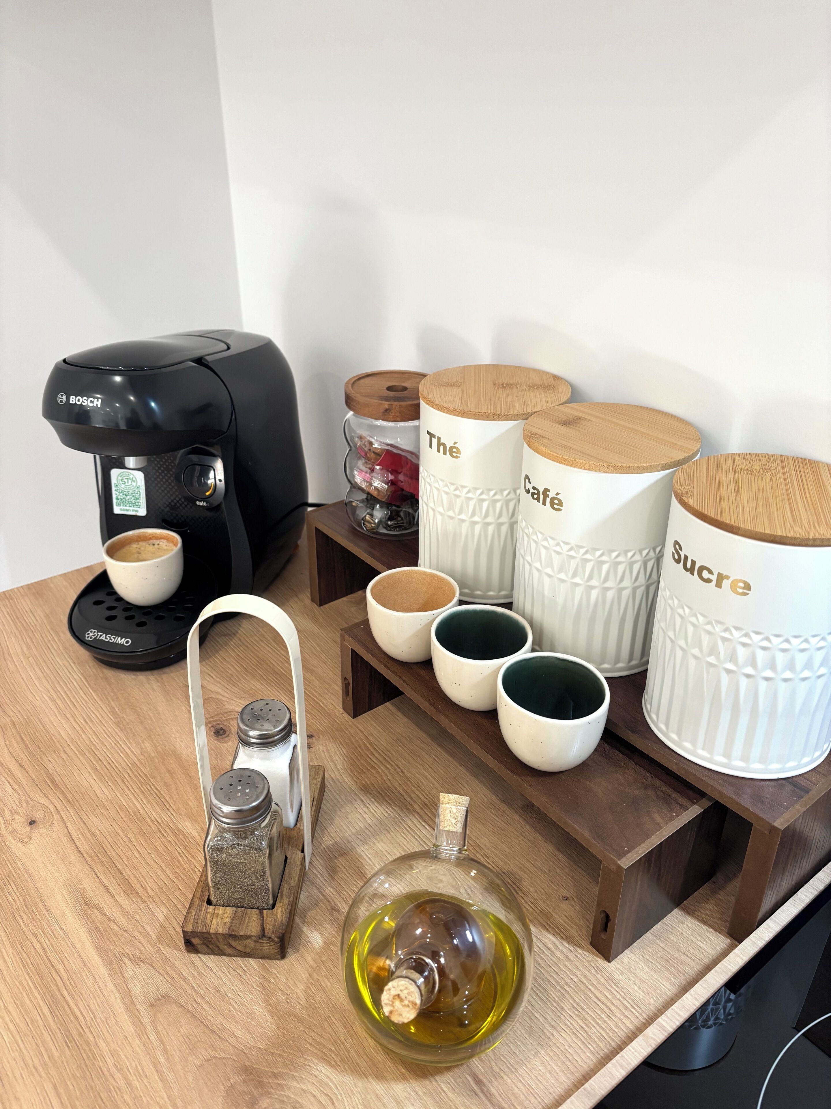 A coffee maker, salt and pepper shakers, a corkscrew, and containers labeled 'The Café,' 'Sucre,' and 'Thé' on a wooden table.