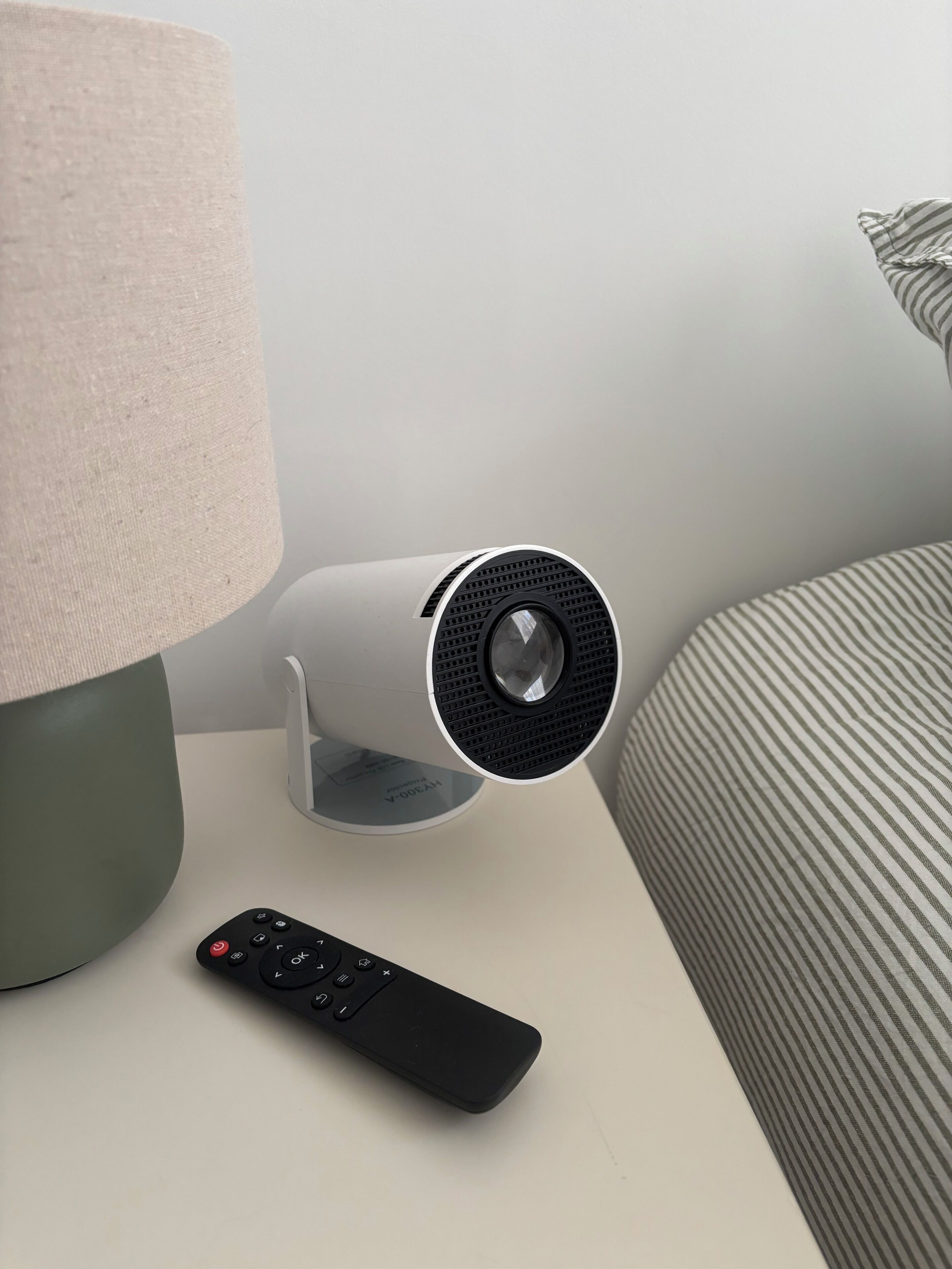 A bedside table with a lamp, a remote control, and a cylindrical speaker.