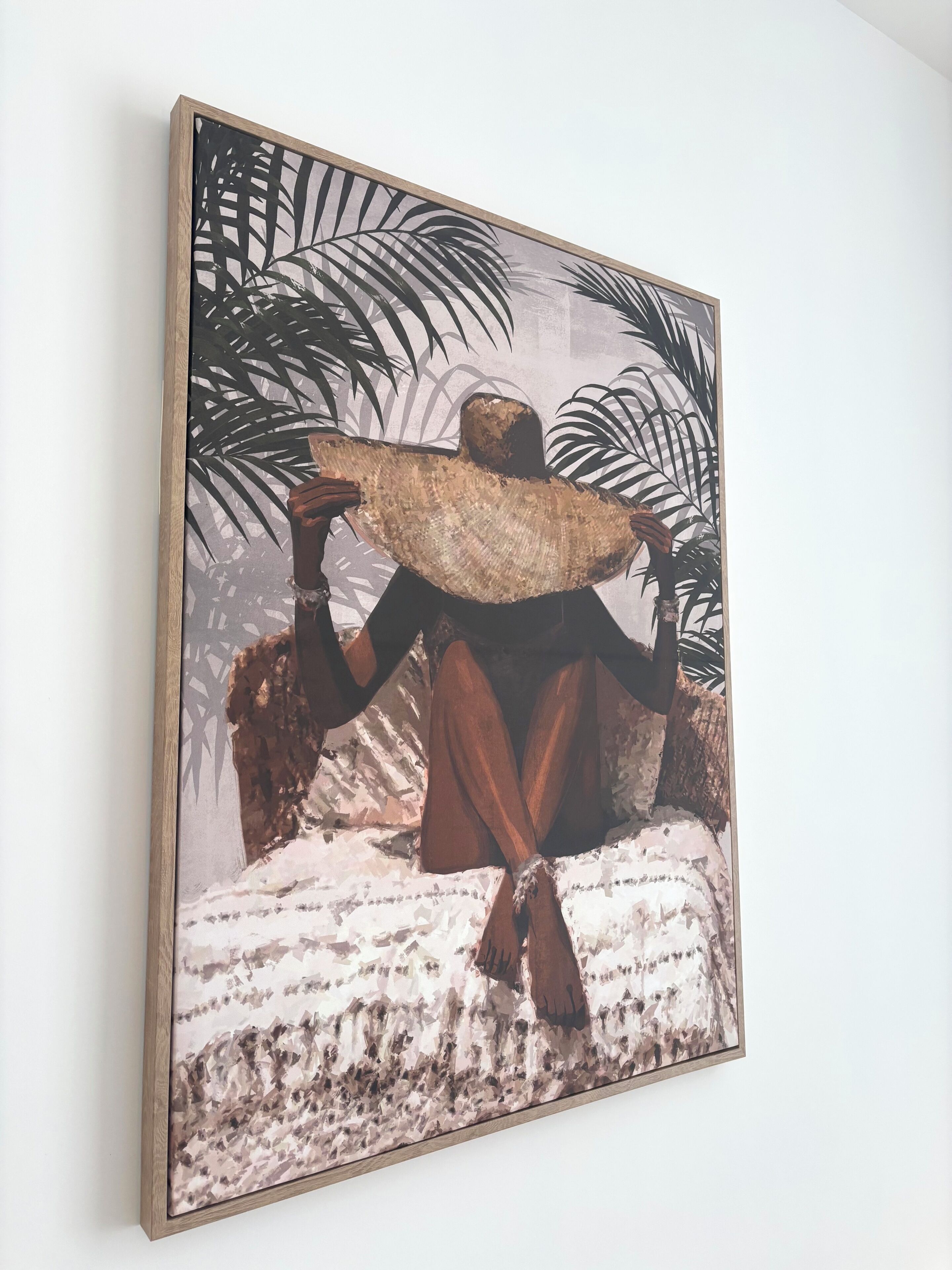 A framed artwork depicting a figure with a large hat, set against a backdrop of palm leaves.