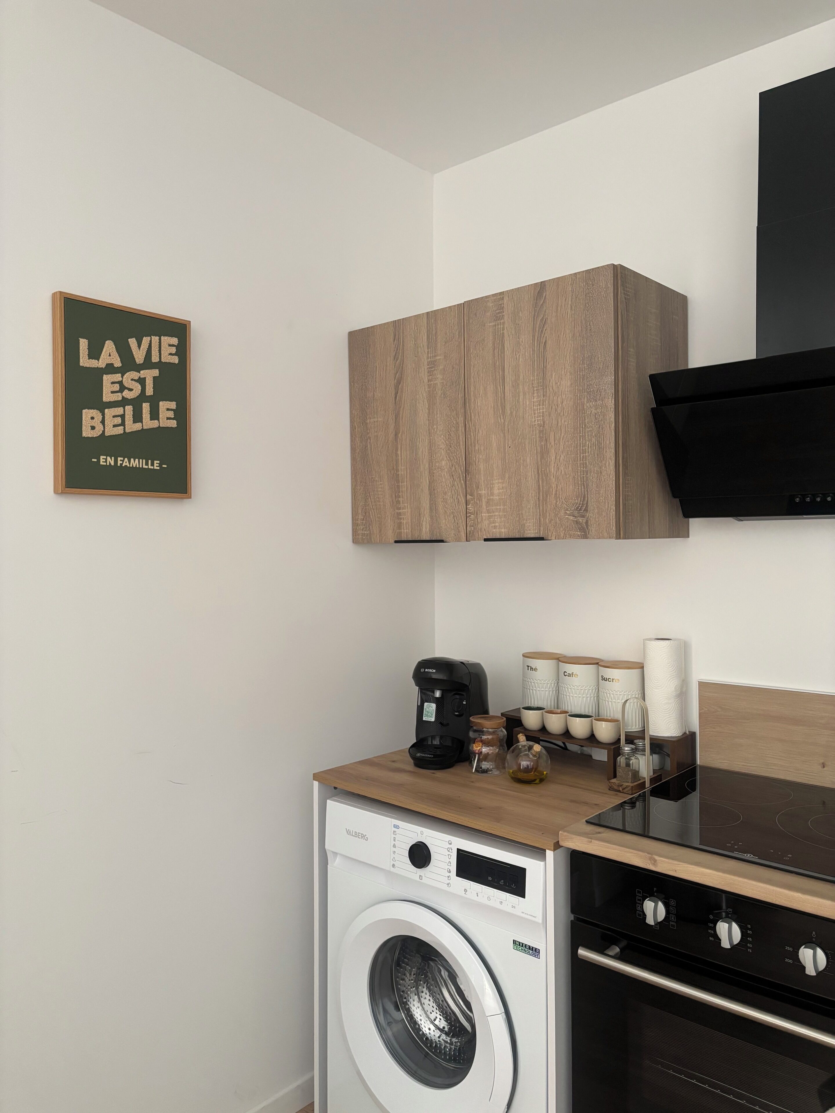 A compact kitchen with a washing machine, a coffee maker, and wooden cabinets.