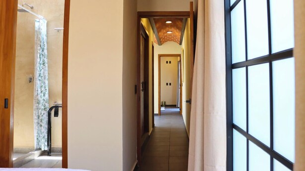 Corridoio di un hotel con doccia, una porta con maniglia, pavimento piastrellato e finestra con griglia.