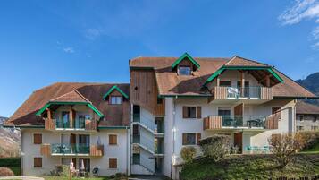 A multi-story building with balconies, a parking area, and a mountainous backdrop.