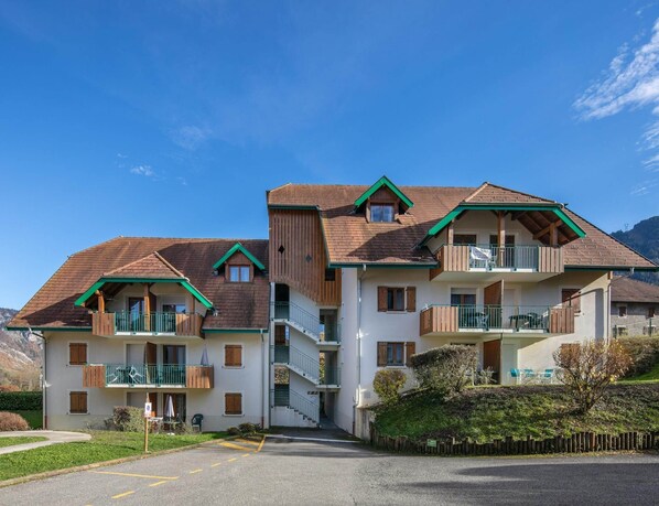 A multi-story building with balconies, a parking area, and a mountainous backdrop. - Duplex for 12 Near Lake Annecy (Giez)