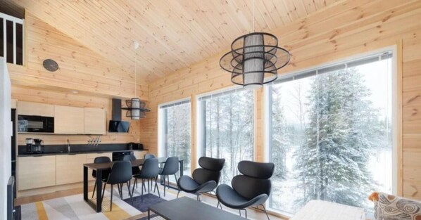 A modern interior with a wooden ceiling, a dining area with chairs, a kitchen with appliances, and large windows with a snowy view.