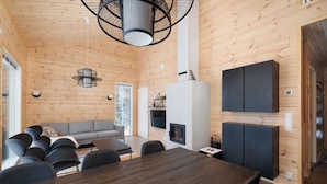 A modern interior with a wooden ceiling, a dining area with a wooden table and chairs, a gray sofa, and a fireplace. - Porevillas Iso-Syöte B | Jacuzzi & Sauna (Syöte)