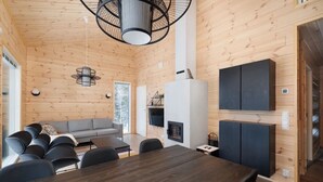 A modern interior with a wooden ceiling, a dining area with a dark wooden table and chairs, a gray sofa, and a fireplace. - Porevillas Iso-Syöte B (Syöte)