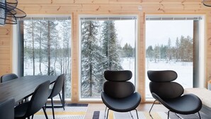 A wooden cabin interior with a dining table, chairs, and a view of a snowy forest through large windows. - Porevillas Iso-Syöte B (Syöte)