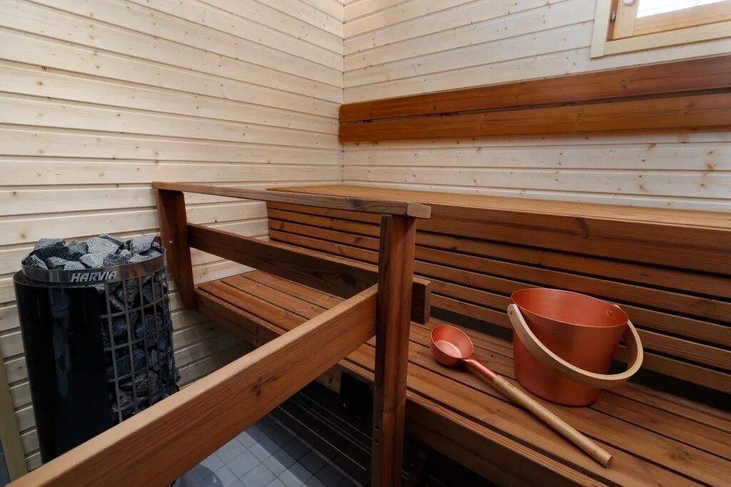 Un sauna avec des bancs en bois, un seau en métal et un récipient perforé.