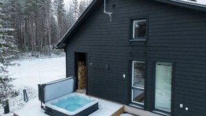 A dark wooden cabin with a hot tub in the snow, a window, and a door. - Porevillas Iso-Syöte B (Syöte)