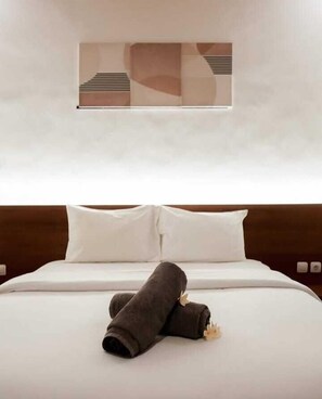 A neatly made bed with white linens and two pillows, a dark brown headboard, and a wall-mounted abstract art piece.