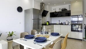 A modern kitchen with white cabinets, a stainless steel refrigerator, a built-in oven, and a dining area with a white table set for four. - Sunstay Benalbeach Juana Flat I Benalmadena (Benalmádena)