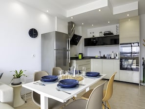 Eine moderne Küche mit weißen Schränken, einem Edelstahlkühlschrank, einem eingebauten Ofen und einem Essbereich mit einem für vier Personen gedeckten Tisch.