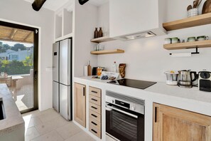 Eine moderne Küche mit Kühlschrank, Backofen und Holzschränken. Darüber befinden sich Holzregale mit verschiedenen Küchenutensilien.