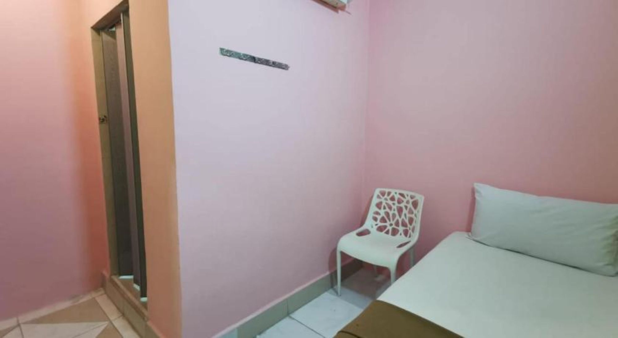 Una habitación pequeña con paredes rosadas, una silla blanca, una cama y una puerta.