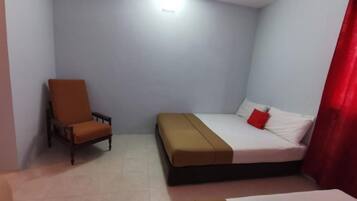 Um quarto de hotel pequeno e simples, com uma cama, uma cadeira e uma mesa de cabeceira.