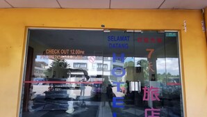 Entrada de un hotel con un amplio ventanal, horario de salida a las 12:00 del mediodía y la frase 'SELANGAT DATANG' escrita en el cristal.
