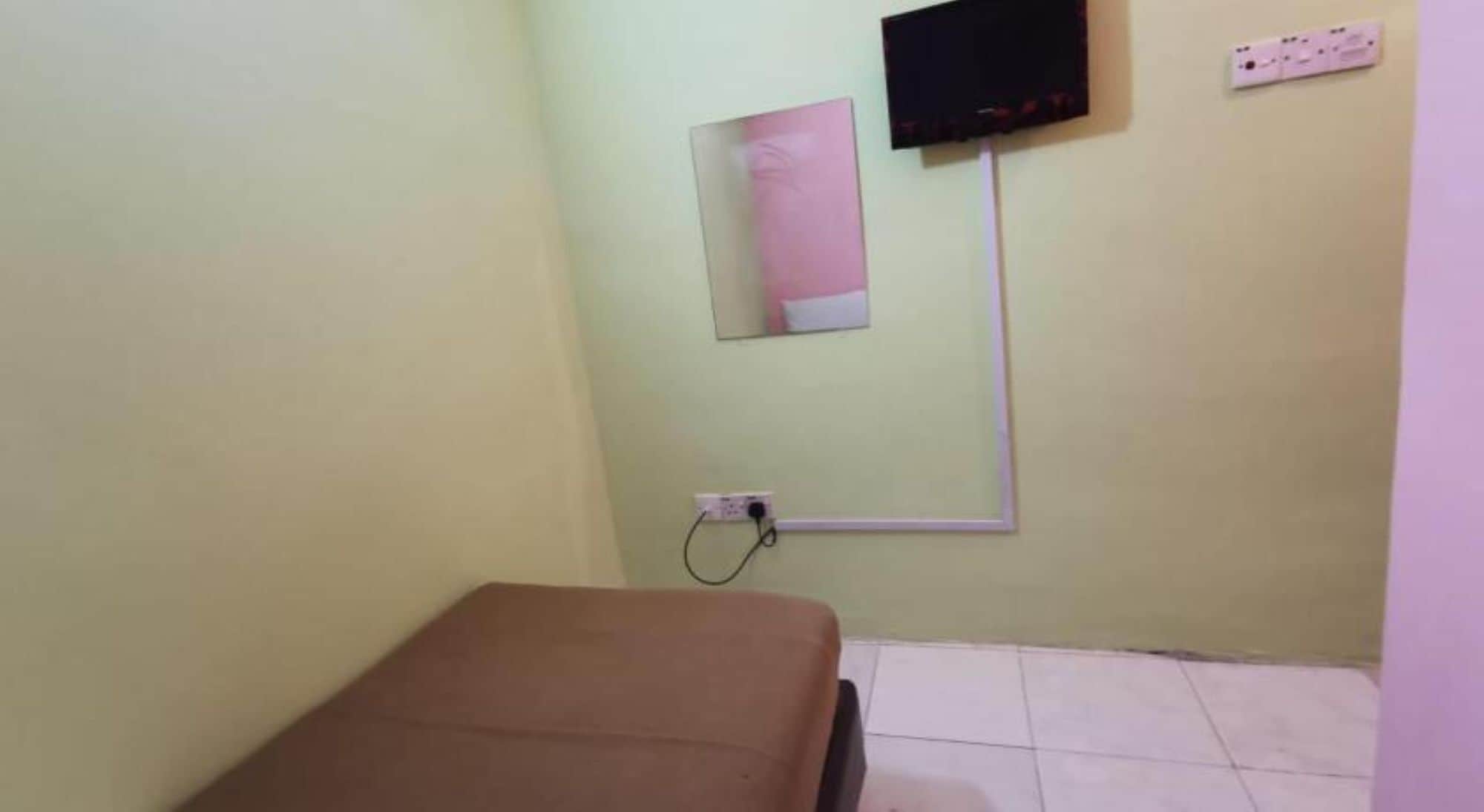 A small room with a bed, a wall-mounted TV, and a power outlet.