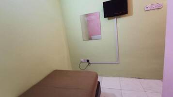 A small room with a bed, a wall-mounted TV, and a power outlet.