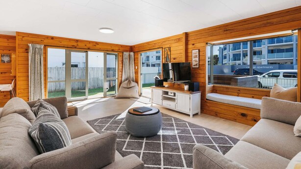 Ein modernes Wohnzimmer mit einer Sofagarnitur, einem Couchtisch, einem TV-Schrank und einem großen Fenster mit Ausblick.