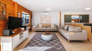 Ein modernes Wohnzimmer mit Sofa, Fernseher und Küchenzeile mit Schränken und einem Fenster.