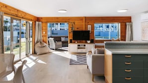 Ein modernes Wohnzimmer mit Fernseher, Sofa und Essbereich, mit Holzwänden und großen Fenstern.