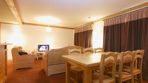 A cozy room with a wooden dining table, chairs, a sofa, and a television. - Appartment in Vaujany (Les Deux Alpes)