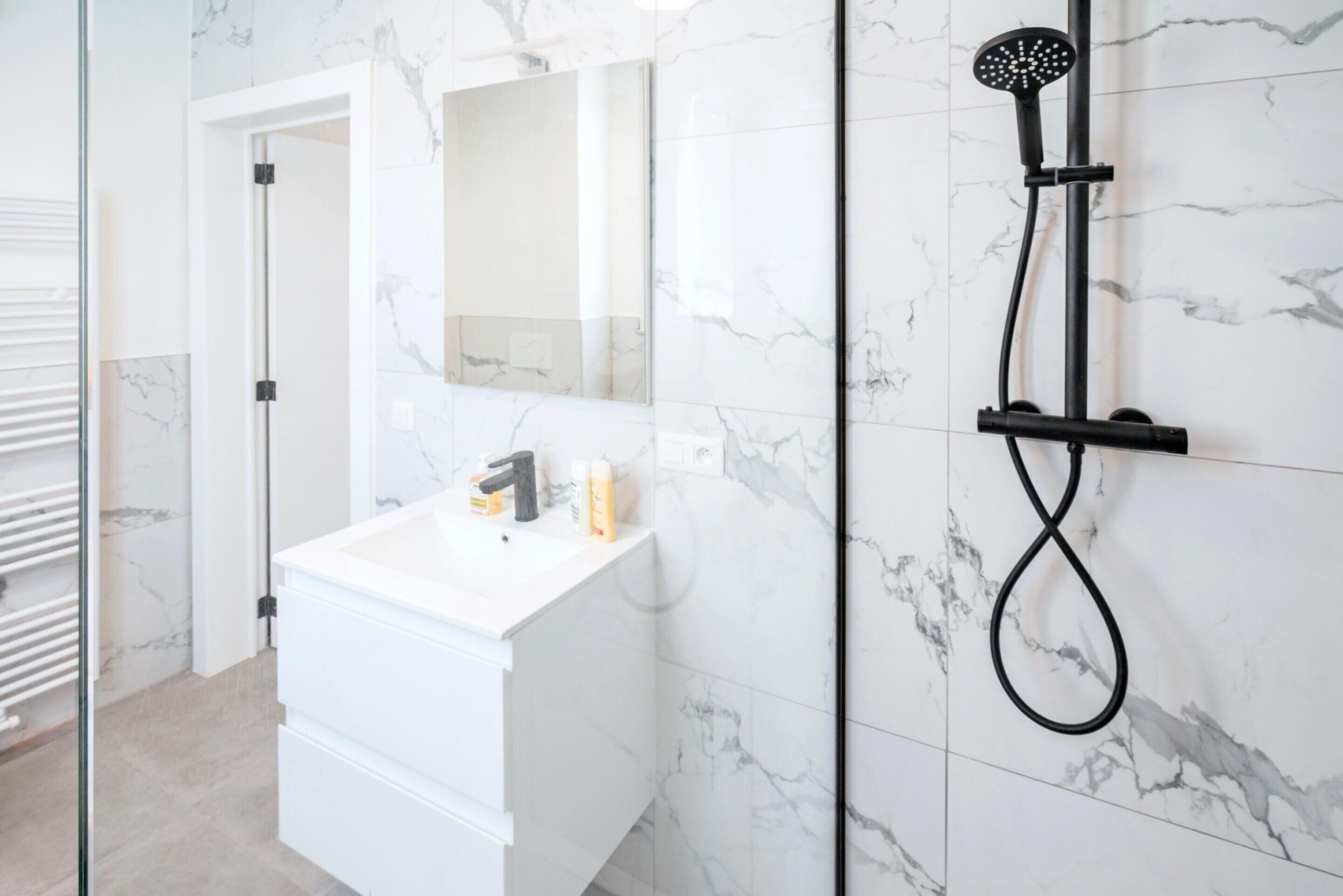 A bathroom with a white vanity, a handheld showerhead, and a mirror.