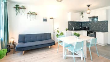 Eine moderne Küche mit weißen Schränken, einer Marmor-Spritzschutzleiste und einem Essbereich mit weißem Tisch und blauen Stühlen.