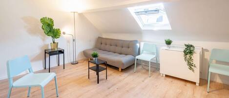 Et loft-agtigt opholdsstue med sofa, to lænestole, et lille bord og en radiator.