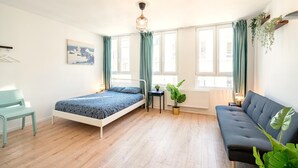 A bedroom with a bed, a sofa, a chair, a small table, a potted plant, and a window with curtains. - Cosy Apartment in Central Antwerp (Antwerp)