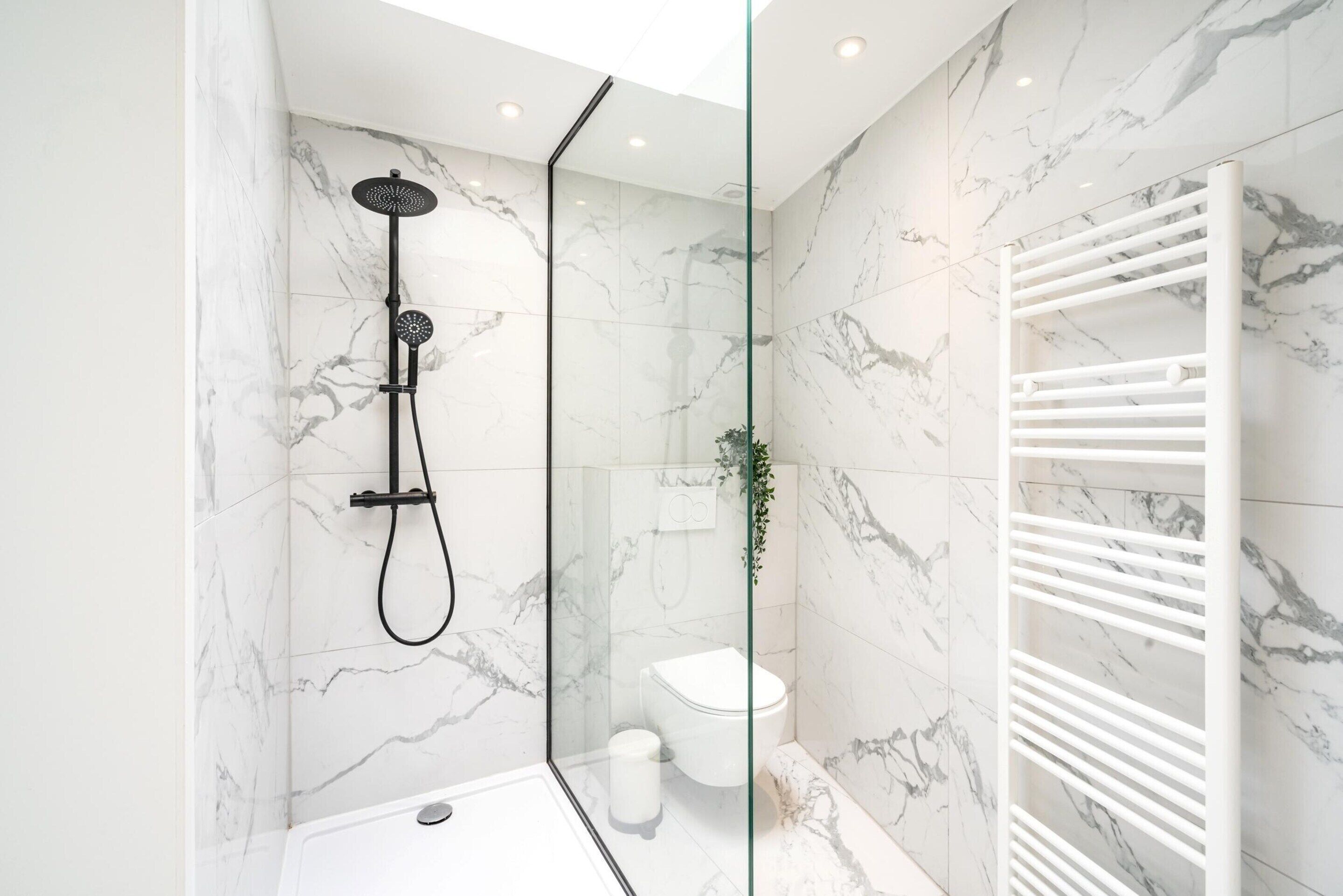 Een moderne badkamer met een glazen douchecabine, een wit toilet en een wand betegeld met marmer.