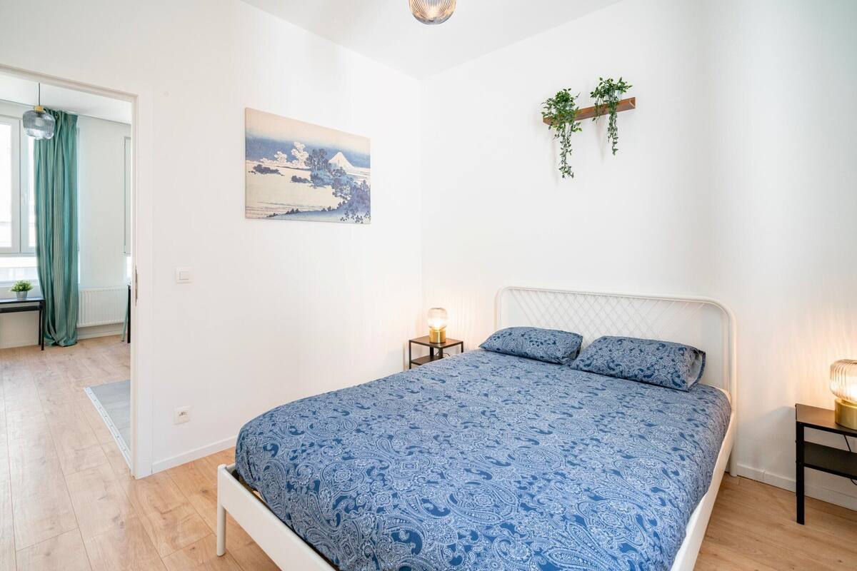 A bedroom with a bed, a bedside table, a wall-mounted plant, and a painting.