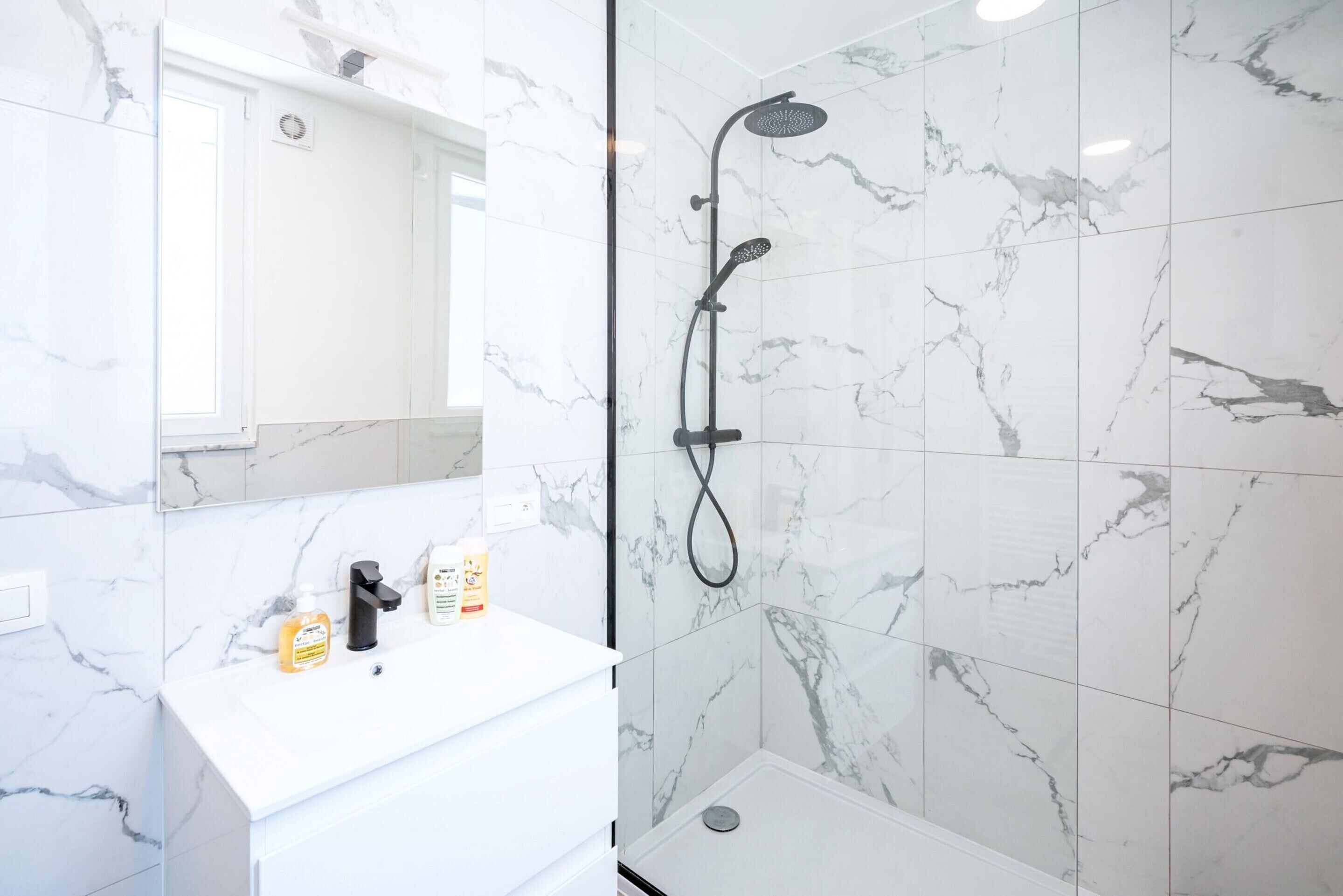 A bathroom with a white marble sink, a handheld showerhead, and a glass-enclosed shower stall.