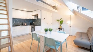 A modern kitchen with white cabinets, a marble backsplash, and a dining area with a white table and blue chairs. - Cosy Apartment in Central Antwerp (Antwerp)