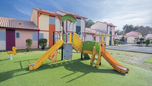 Un parque infantil con toboganes y estructuras para escalar frente a una hilera de casas con techos de tejas rojas.