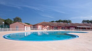 Una piscina con un borde pavimentado, un edificio de techo rojo y un área cercada.