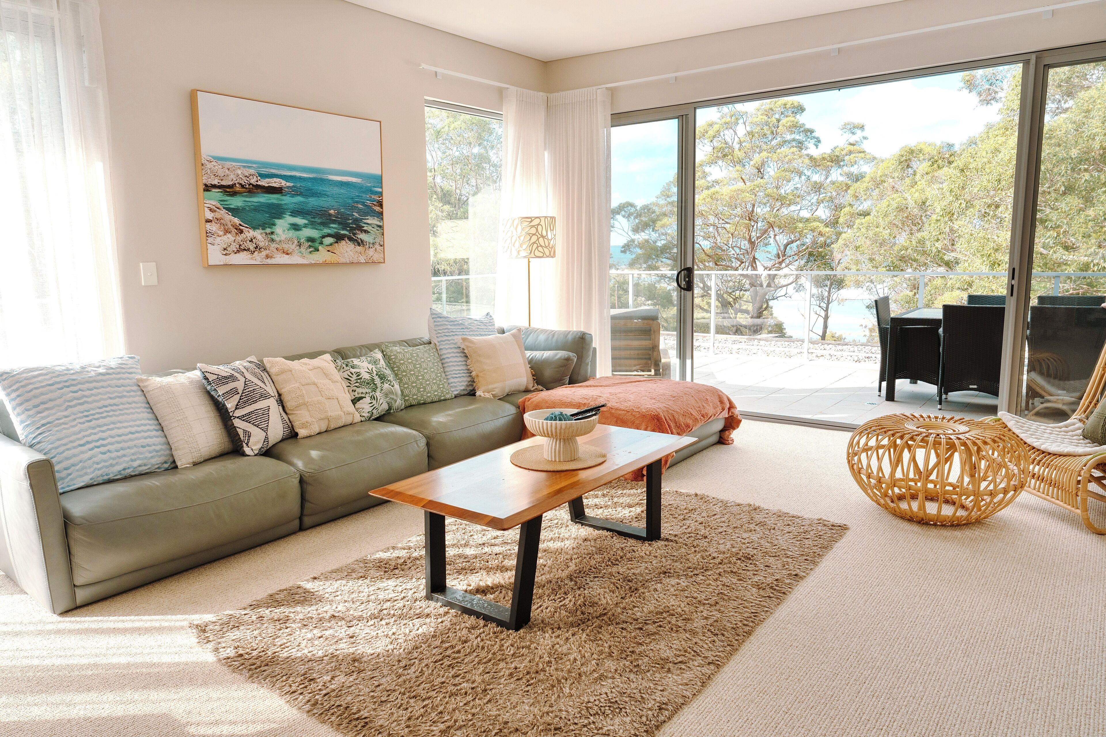 A living room with a sofa, a coffee table, a wicker chair, and a view of the outdoors through large glass doors.