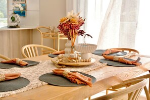 A dining table set with placemats, folded napkins, and a centerpiece with flowers. - 3BR Beachfront Penthouse in Huskisson – Jervis Bay (Huskisson)