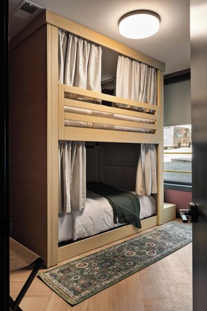 Ein Stockbett mit Vorhängen, ein gemustertes Teppich und eine Deckenleuchte.